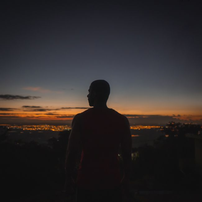 Silhouette of a man gazing at a vibrant sunset with city lights glowing in the distance. Captivating urban skyline scene. Silhouette of a man gazing at a vibrant sunset with city lights glowing in the distance. Captivating urban skyline scene.