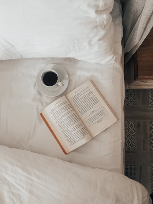 Book and cup of coffee on bed