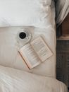 Book and cup of coffee on bed