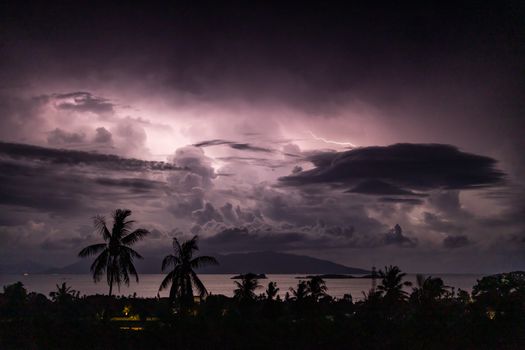 Photo by Balazs Simon A striking view of lightning illuminating dark clouds above a tropical ocean landscape.