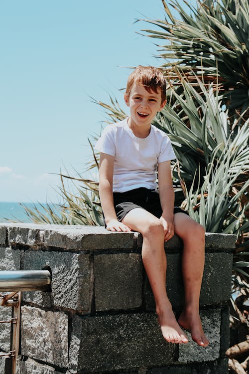 Photo of a Boy in a White Shirt Sitting on a Concrete Surface