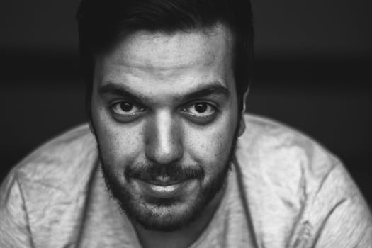 一张黑白特写肖像，描绘了一位面部毛发浓密、目光犀利的年轻人