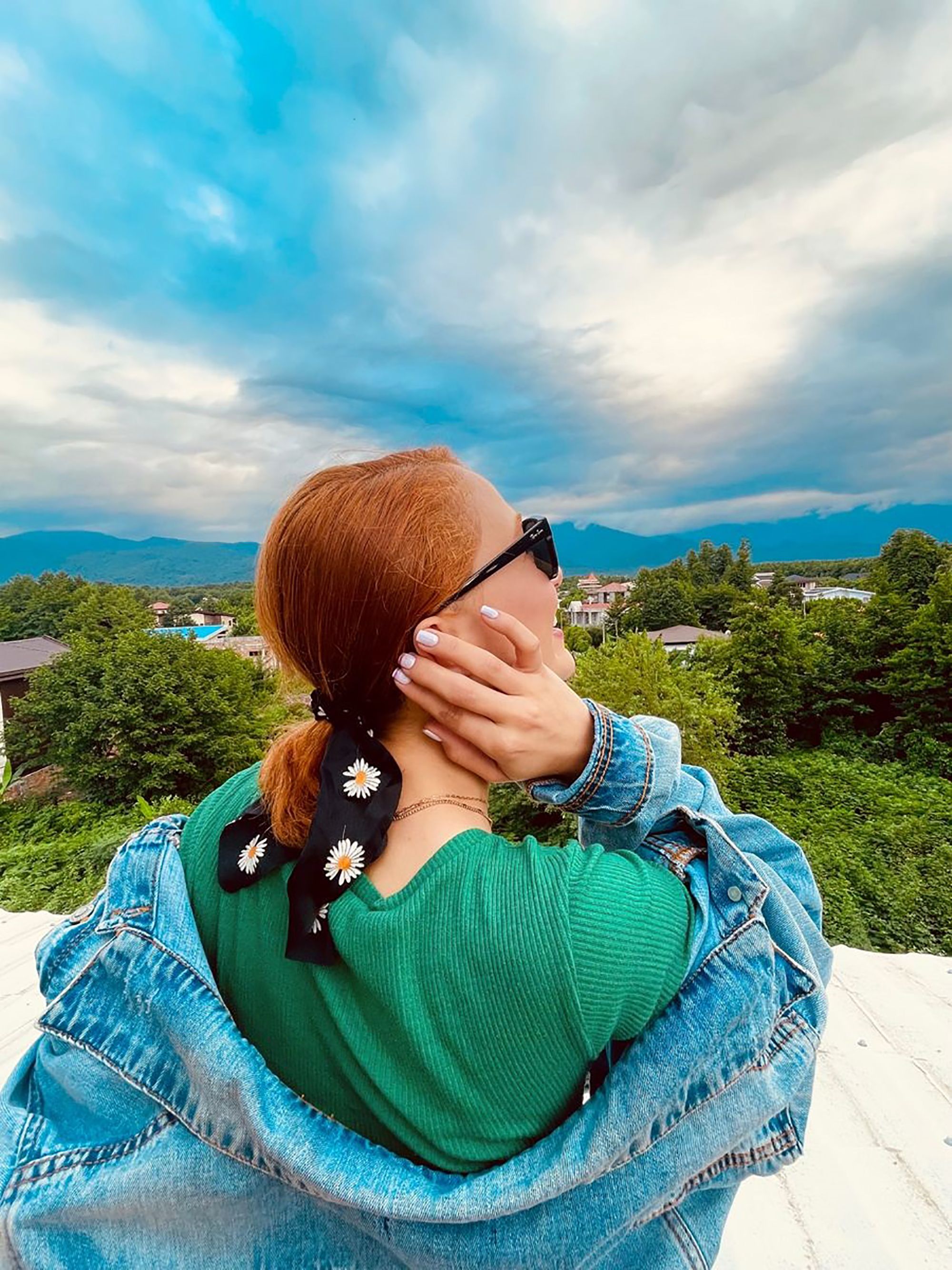 A woman with sunglasses and denim jacket enjoying a scenic outdoor view.
