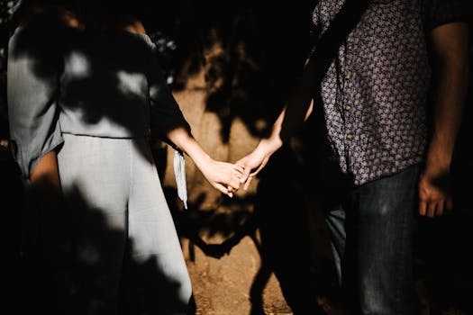 Romantic couple holding hands, capturing intimate shadows and sunlight outdoors.