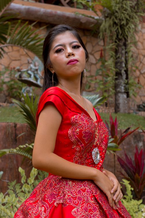 Free Woman in a stunning red gown posing confidently in a lush garden. Stock Photo