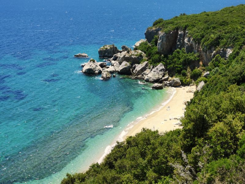Aerial view of a secluded beach in Greece with clear blue waters and lush green cliffs
