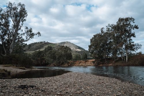 Free Tranquil lakeside scene with rocky shore and trees under a cloudy sky in Victoria, Australia. Stock Photo