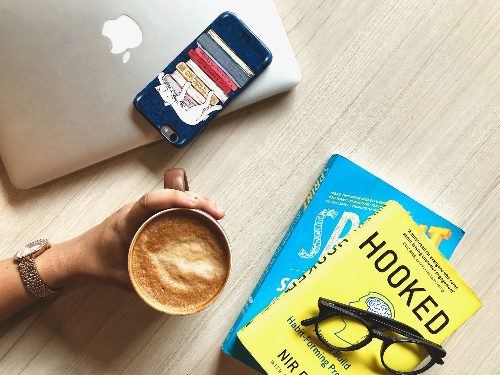 Books, a smartphone, a laptop and a cup of coffee on a light wooden table