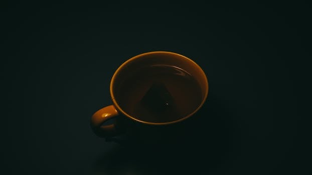 深色背景下的茶杯特写中，有一个浸入的茶袋