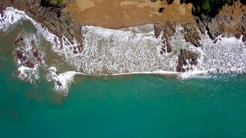 Free Stunning aerial shot of waves crashing on a rocky beach in Costa Rica's lush landscape. Stock Photo