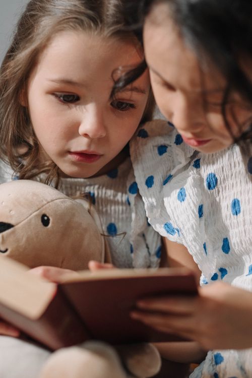 Free Two girls reading a book together, holding a stuffed animal, capturing friendship and learning. Stock Photo