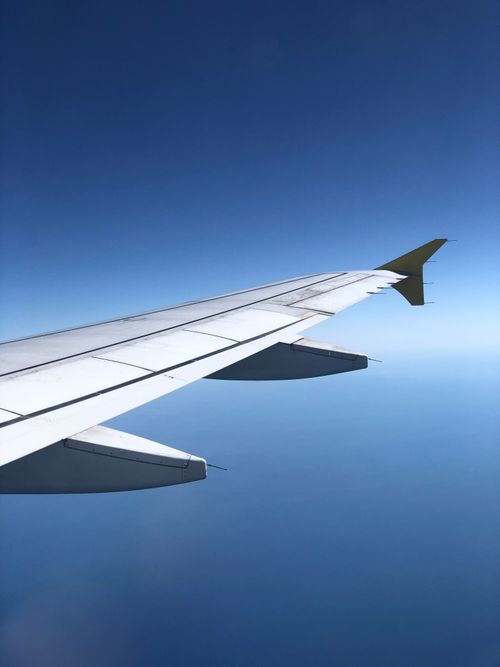 Free View of an airplane wing flying above clouds with a clear blue sky Stock Photo