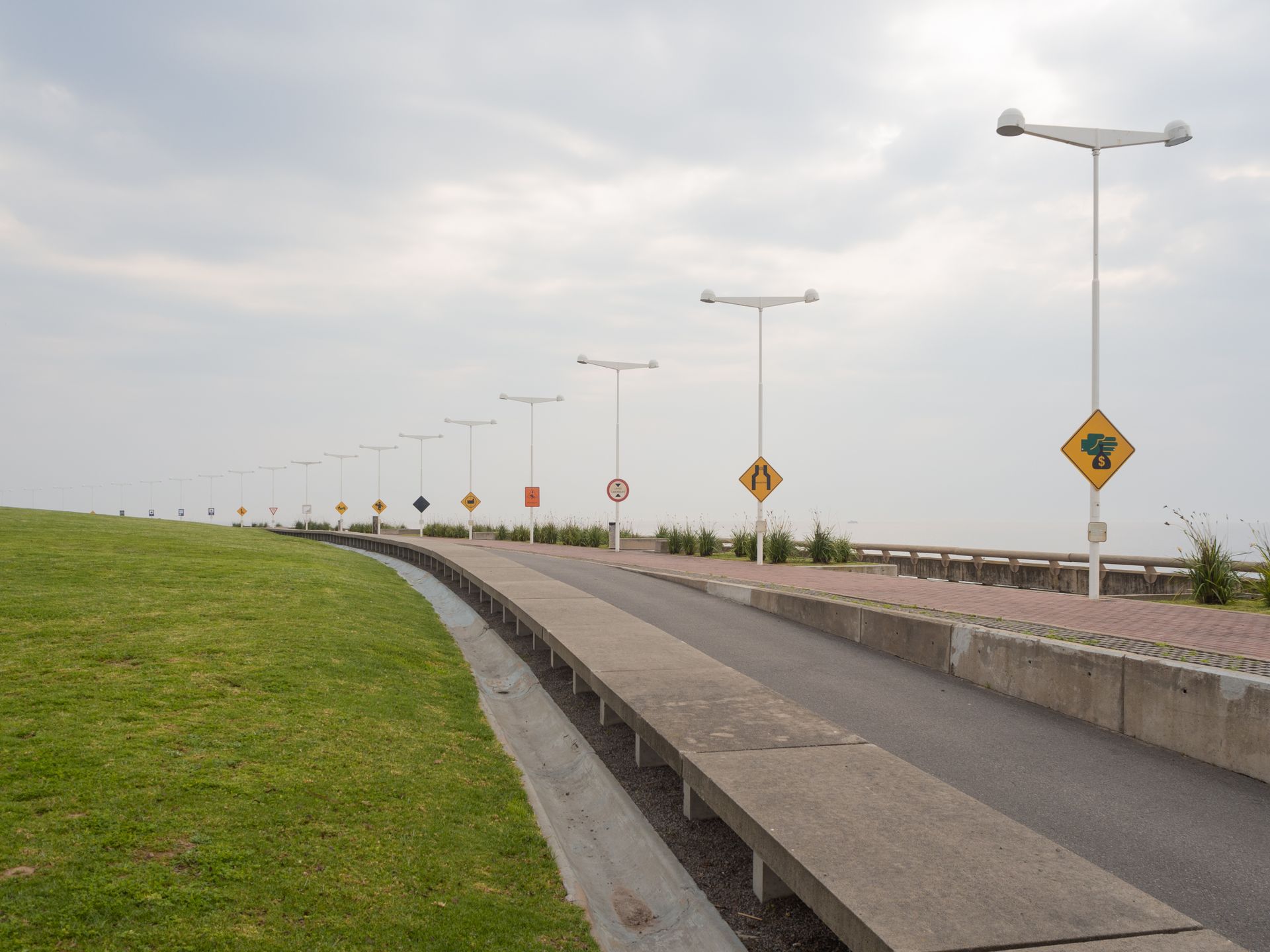 Empty coastal sidewalk with lamp posts and traffic signs on a cloudy day.