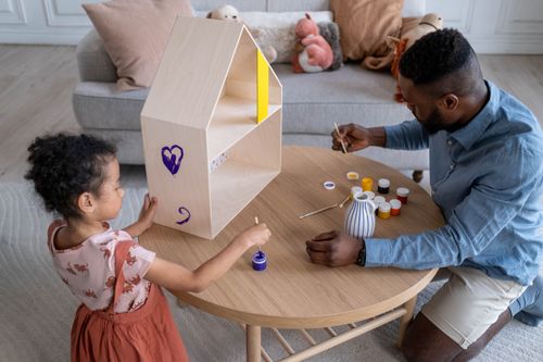 Free A father and daughter enjoy painting a wooden dollhouse together indoors. Stock Photo