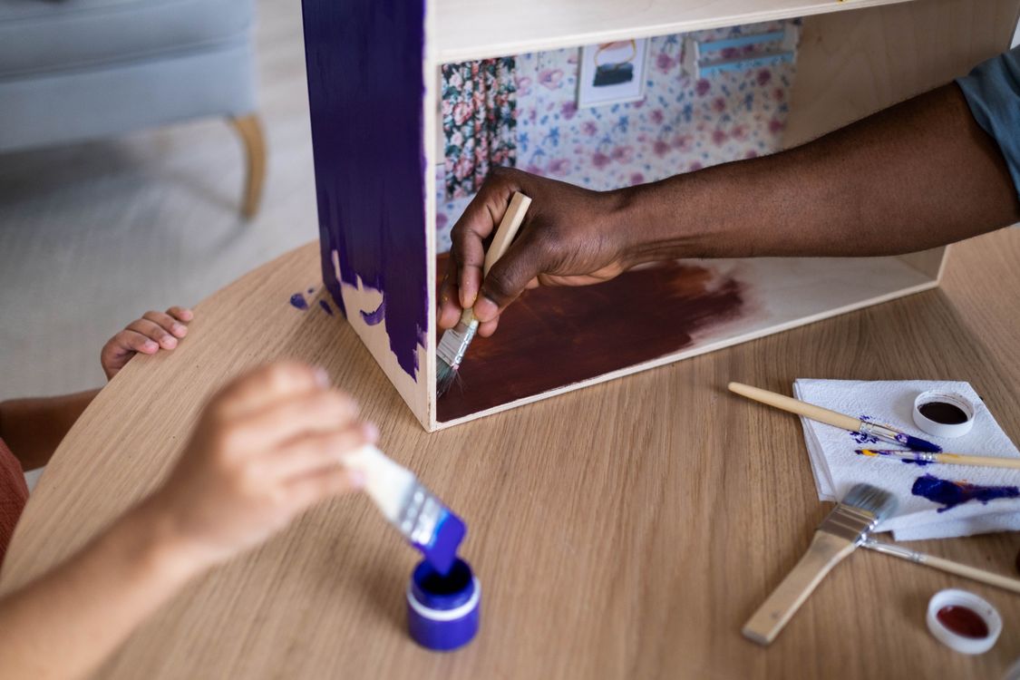 Free Adults and child creatively painting a wooden dollhouse using vibrant colors and brushes. Stock Photo