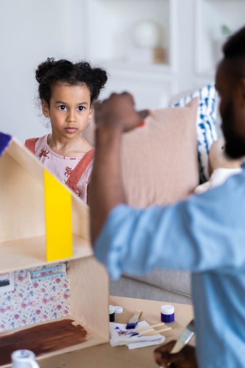 Free A child attentively watches as an adult assists in a craft project indoors. Stock Photo