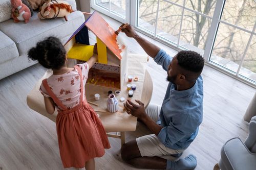Free A father and daughter enjoy painting a dollhouse at home, fostering creativity and bonding. Stock Photo