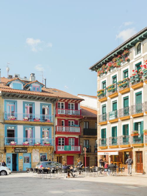 Free Charming town square with colorful homes, balconies, and street cafes in a European setting during a sunny day. Stock Photo