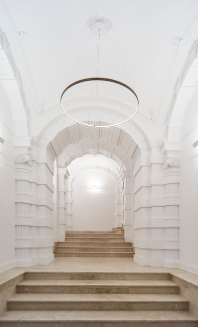 Bright and minimalistic white stairway with a circular chandelier and classical architecture.