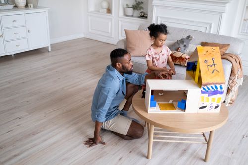 Free A charming family moment as a father and daughter engage with a dollhouse in their living room. Stock Photo