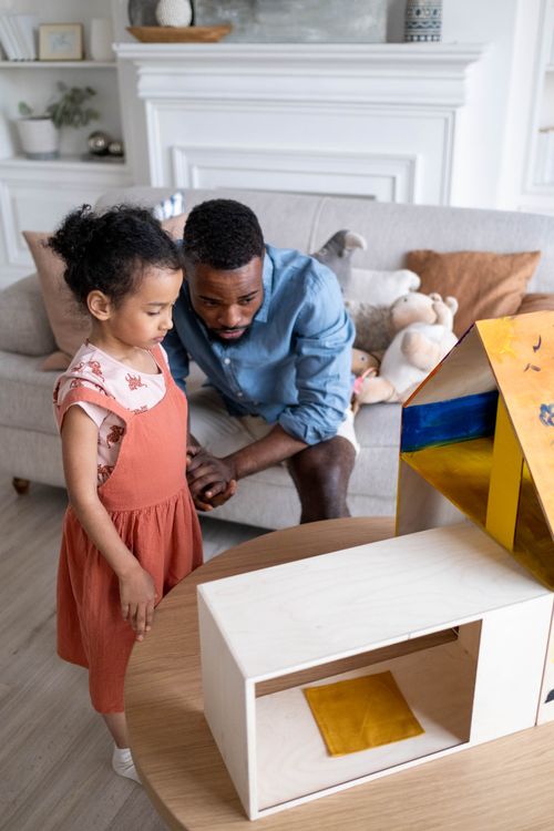 Free Father and daughter engaged in creative play with a toy house indoors, fostering imagination. Stock Photo