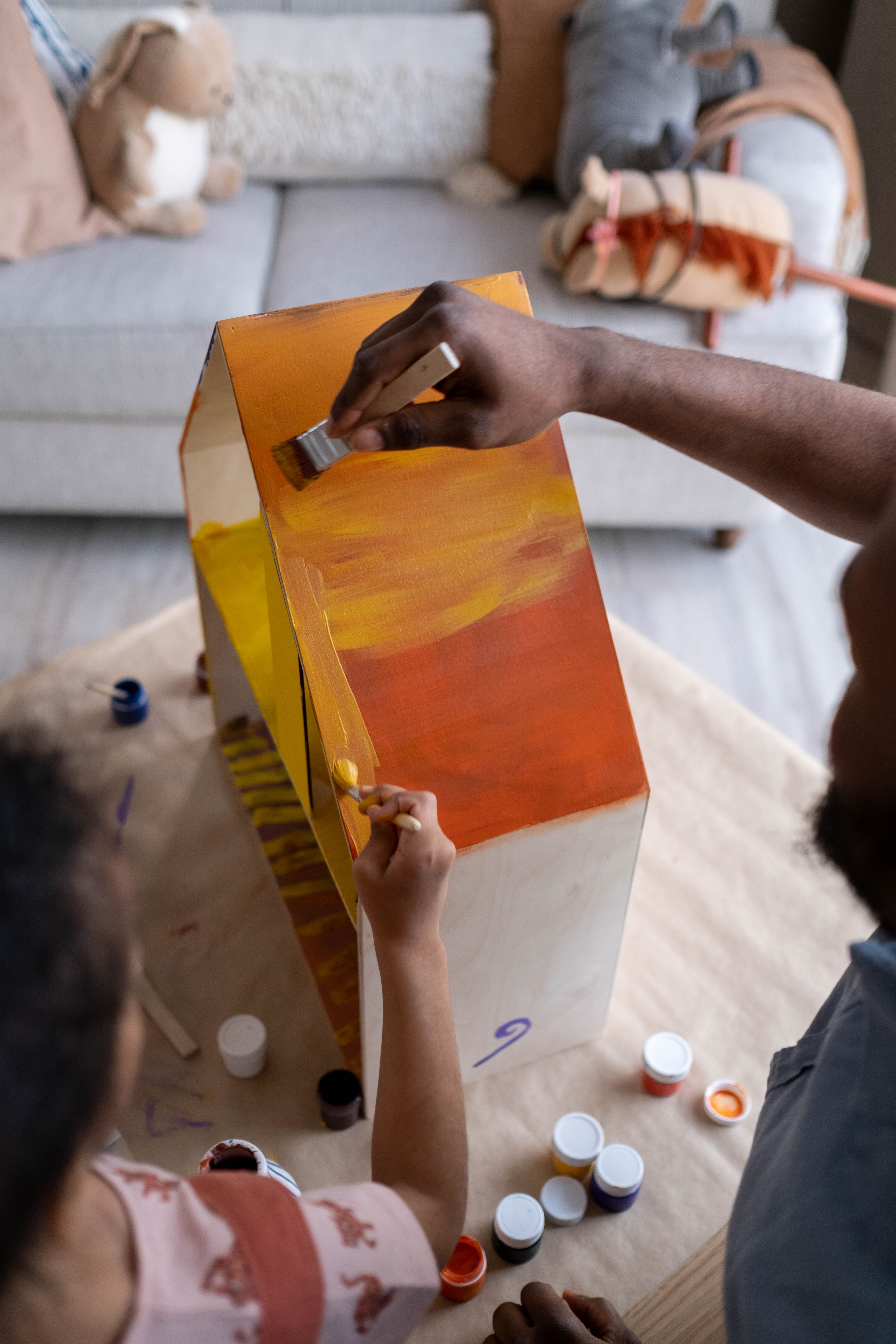 A father and child engage in a creative arts and crafts activity, painting a dollhouse indoors.