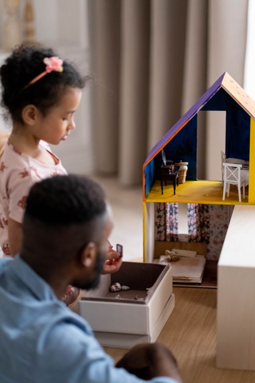 Free A father and his daughter enjoy bonding time playing with a dollhouse indoors. Stock Photo