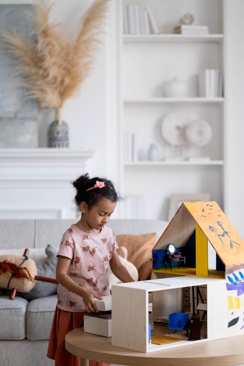 Free Young girl enjoying playtime with a dollhouse in a homely living room setting. Stock Photo