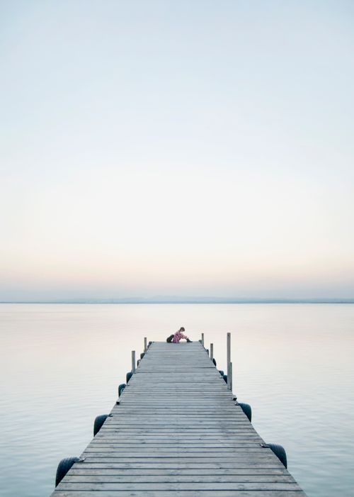 Free A serene view of a pier stretching into the calm ocean under a pastel sunrise sky. Stock Photo