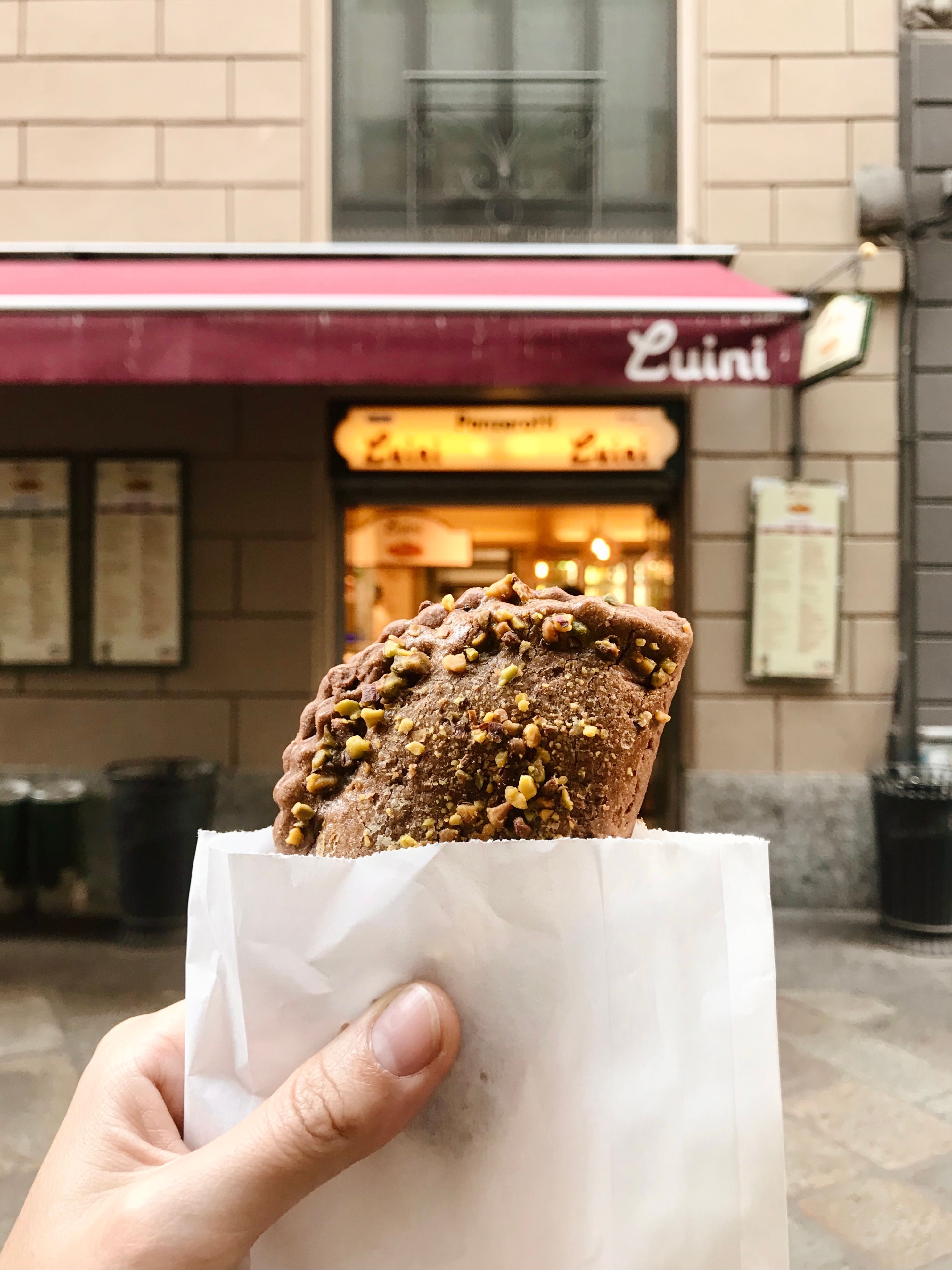 Freshly baked pastry held outside Luini bakery in an urban setting.