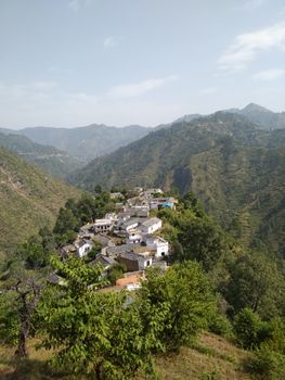 A beautiful aerial view of a village surrounded by lush green mountains under a clear sky. - Fotografer Sidoarjo