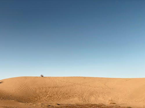 People Sitting on a Dune and Footprints on Sand