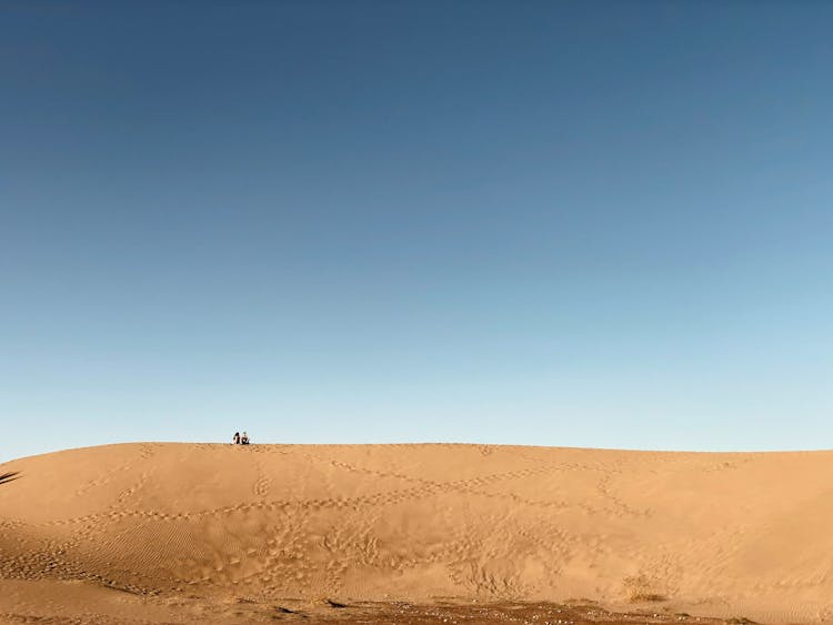 People Sitting On A Dune And Footprints On Sand