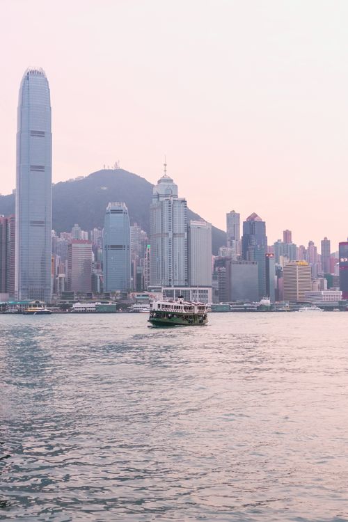 Free Tranquil scene of Victoria Harbor with iconic Hong Kong skyline, ferry, and mountains at sunset. Stock Photo