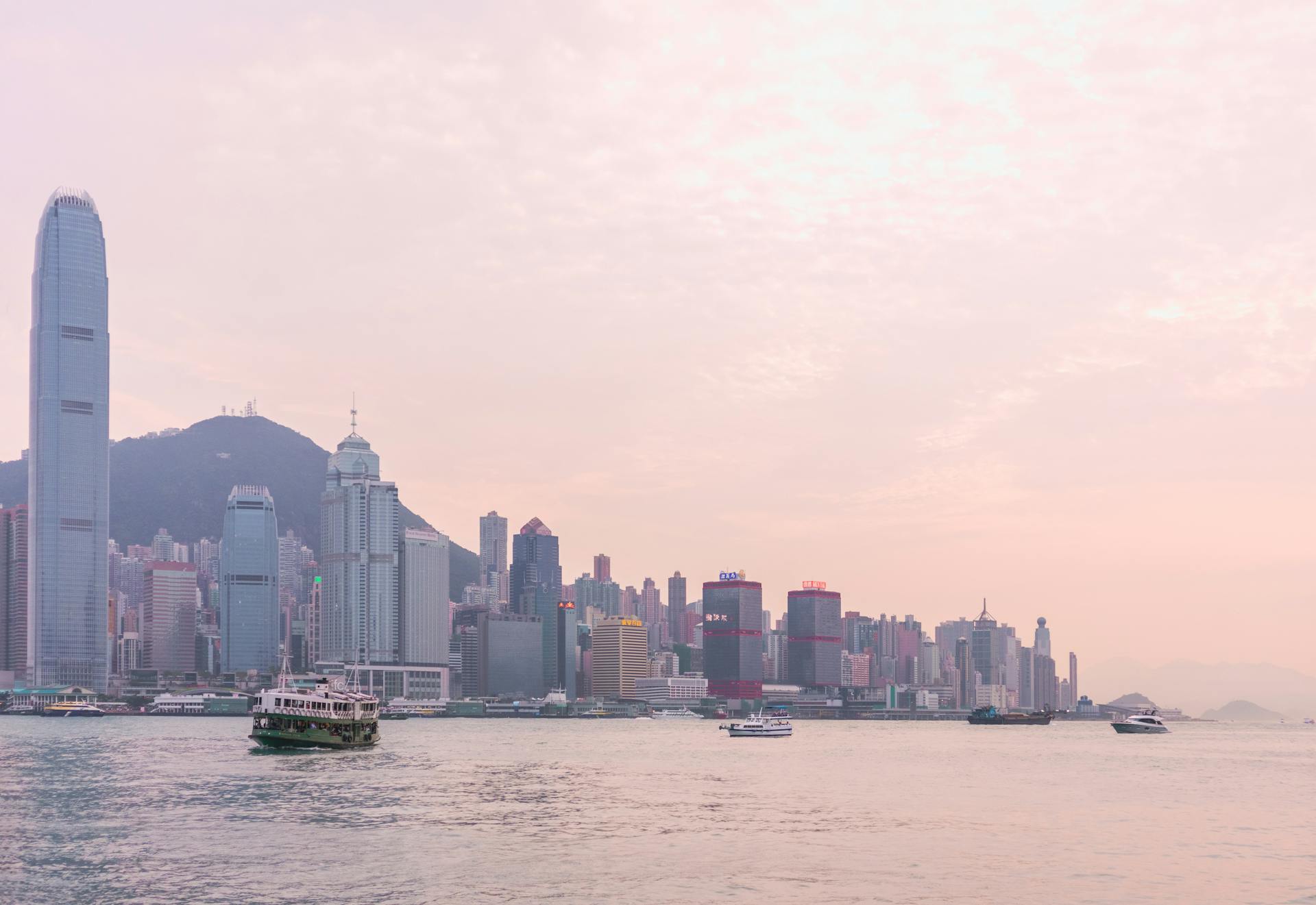 Serene view of the Hong Kong skyline at sunset with boats on Victoria Harbour.