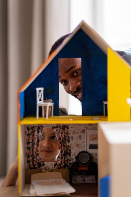 Free Portrait of a father and daughter enjoying playtime with a colorful dollhouse indoors. Stock Photo