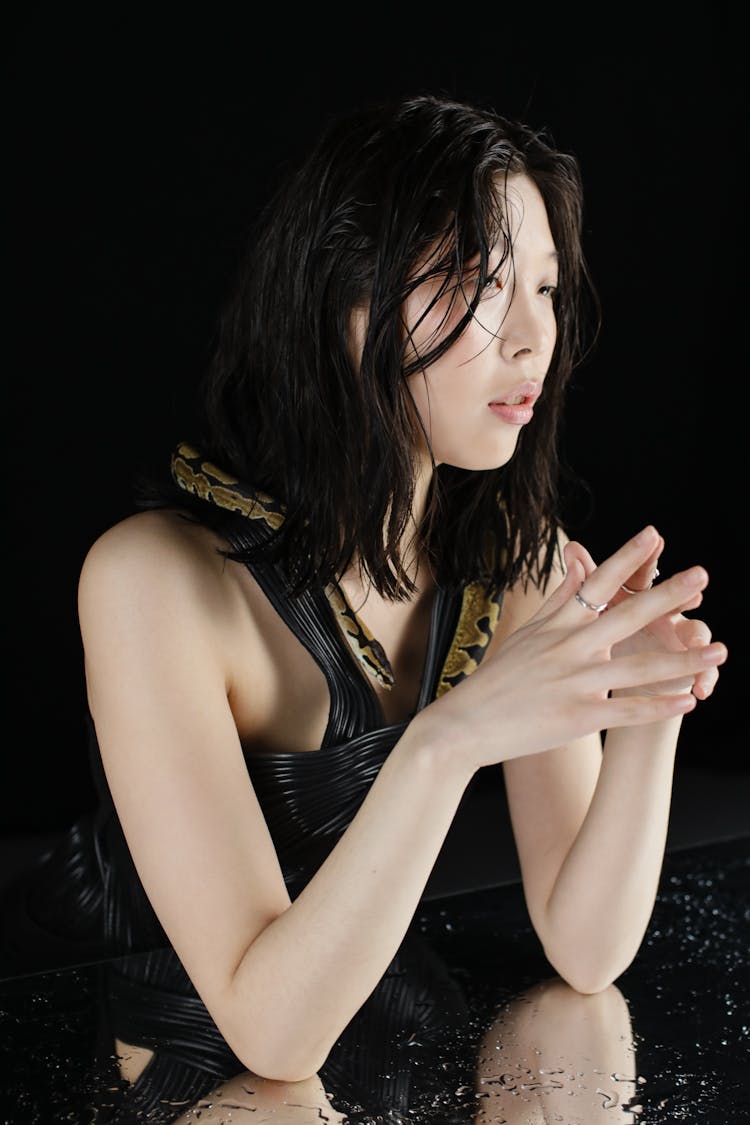 Young Woman With A Snake Around Her Neck Leaning On A Table With A Wet Mirror Top