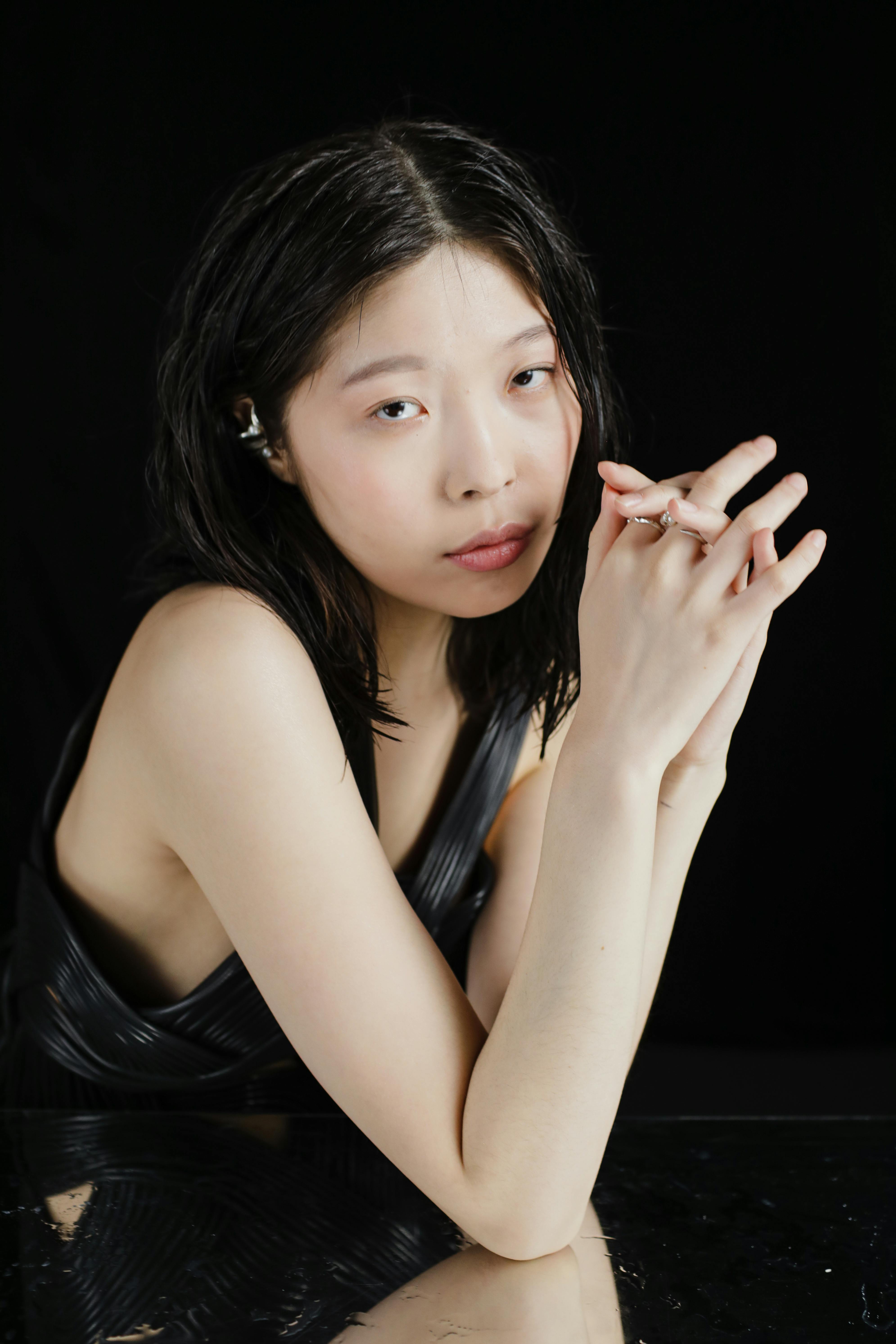 Stylish portrait of a woman posing with hands together against a black background.