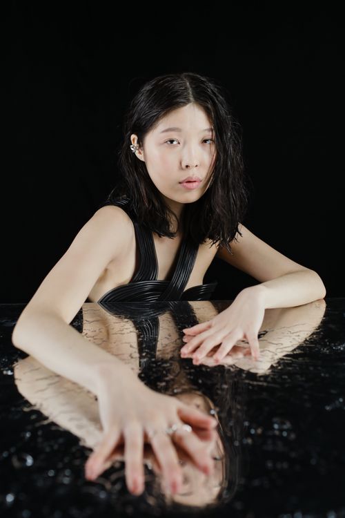 Free Artistic portrait of a woman in a black top reflected on a dark surface, with a mysterious and moody atmosphere. Stock Photo