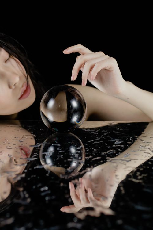 Free Artistic portrait of a woman with a crystal ball reflecting on a wet surface. Stock Photo