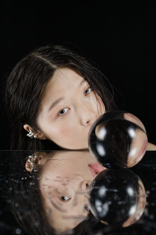 Free Striking close-up of a woman with a crystal ball and mirror reflection, set against a black background. Stock Photo