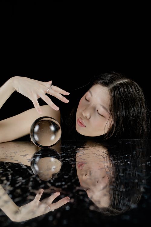 Free An enigmatic portrait of a woman with a crystal ball on a dark reflective surface. Stock Photo