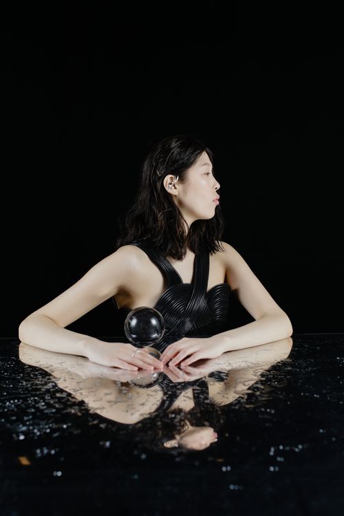 Free An enigmatic woman with a crystal ball on a reflective glass table in a studio. Stock Photo