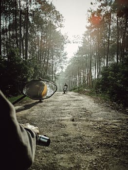 A motorcyclist rides along a dirt road surrounded by trees in natural sunlight.