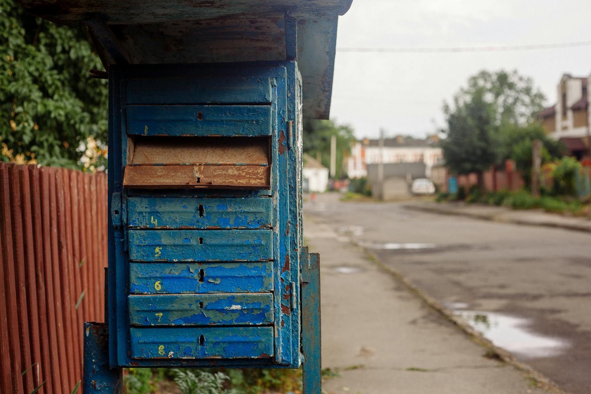 Rustic blue mailbox on a city street, showing signs of age and weathering.