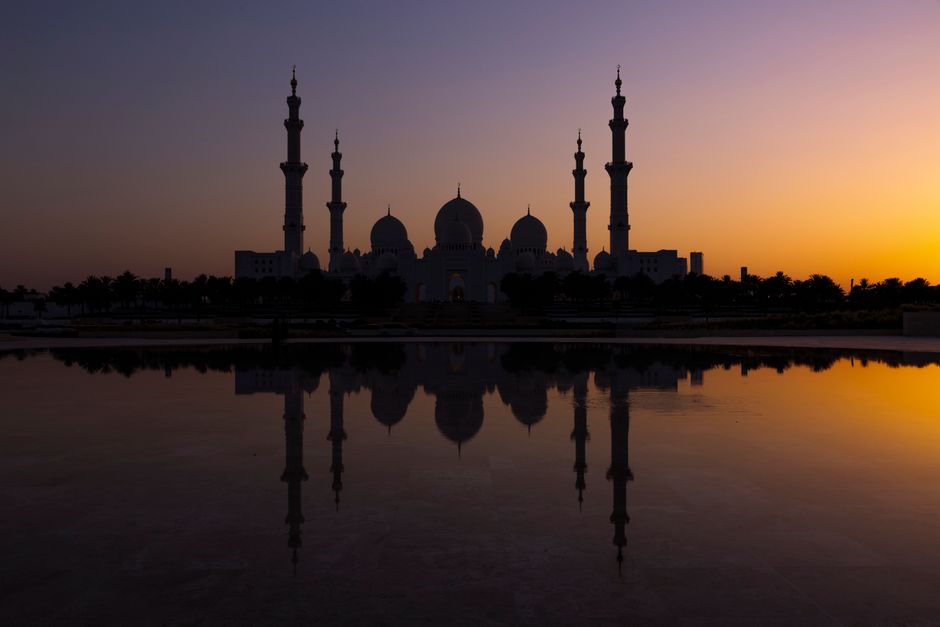 Silhouette of Sheikh Zayed Grand Mosque reflecting in water during a vibrant sunset in Abu Dhabi.