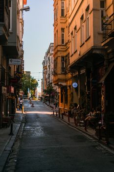 Picturesque narrow street lined with historic buildings, outdoor cafés, and shops under a clear blue sky.