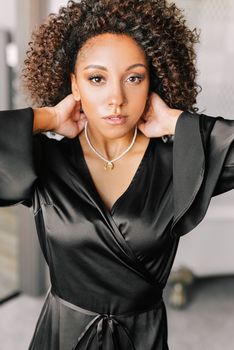 Graceful woman in black satin dress posing confidently indoors