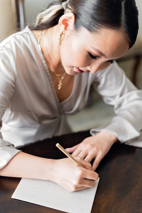 A Woman in White Long Sleeves Writing on Paper