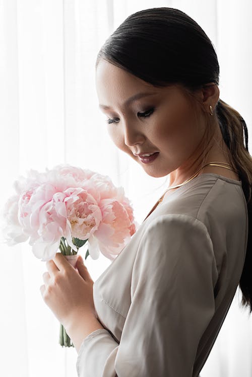 Free Woman Standing Near the White Curtain Holding a Bouquet of Flowers Stock Photo